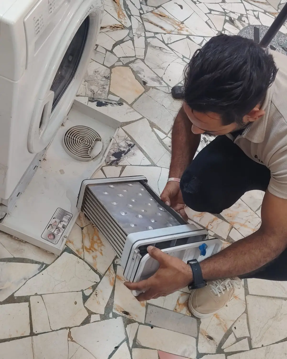 فني من شركة إي جي يطلّع وحدة التكثيف من أسفل مجفف ملابس لفحصها.